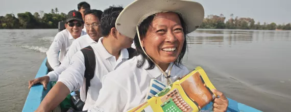 Image of people in a boat in Cambodia holding poster with information about treatment of leprosy