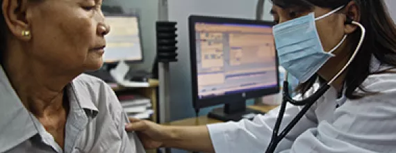 Physician wearing a mask, with a stethoscope listening to a female patient's heart