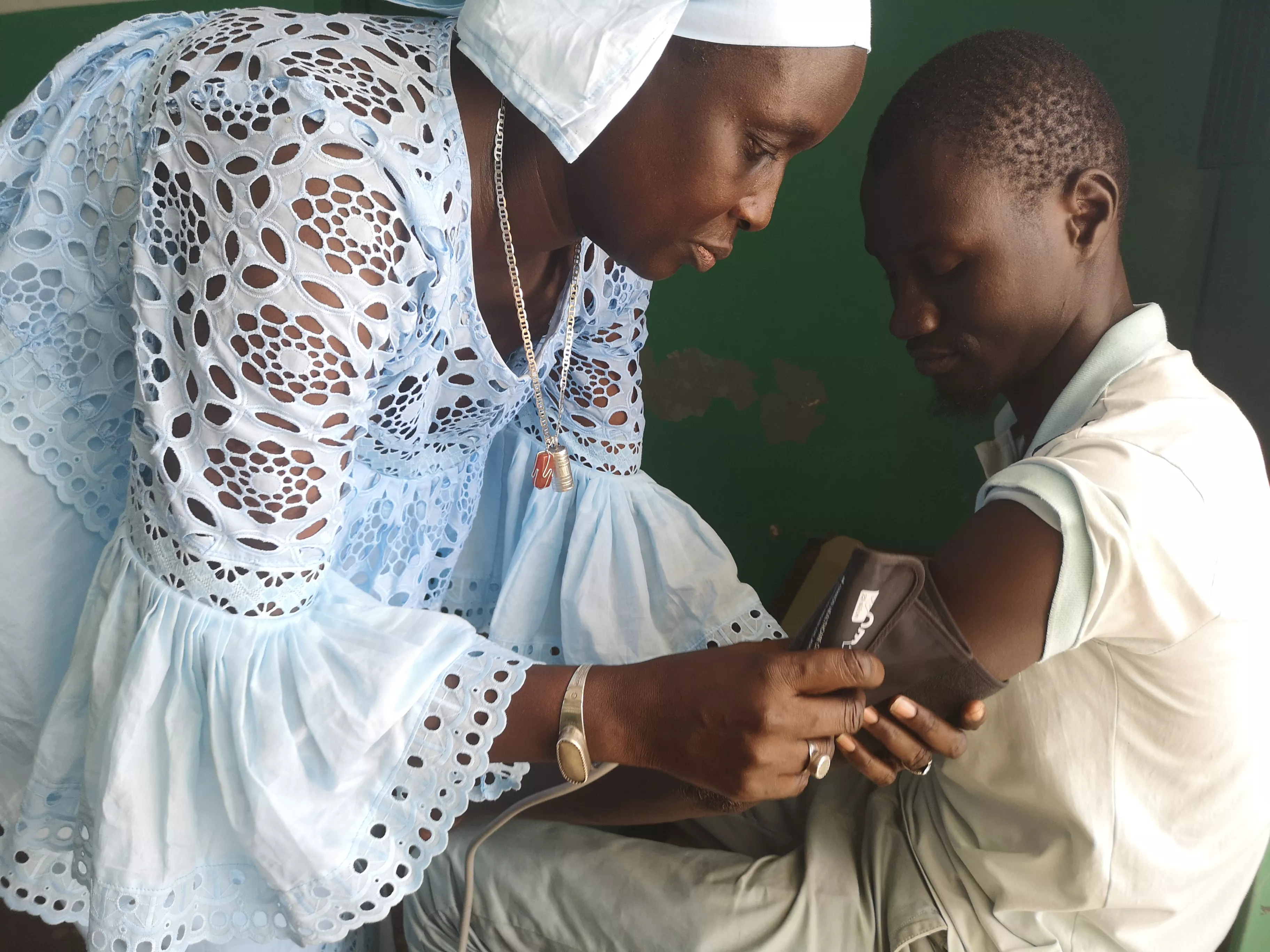 Female community health worker measuring blood pressure of a boy in Dakar