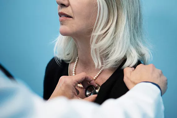 Physician with a stethoscope listening to a female patient's heart