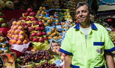 Image of a fruit seller standing in front of a fruit stand