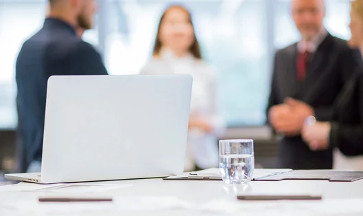 Laptop laying on a meeting room table with blurry business people in the background