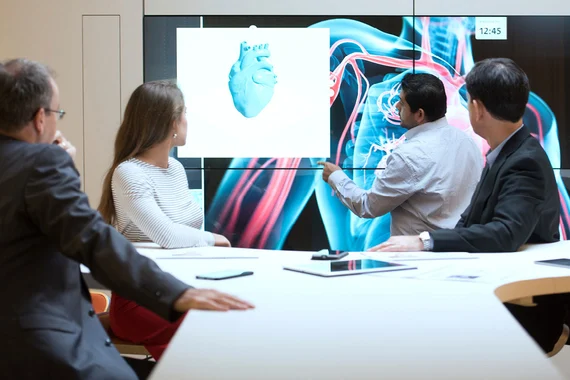 Business people in a meeting room watching a screen displaying a 3D generated heart