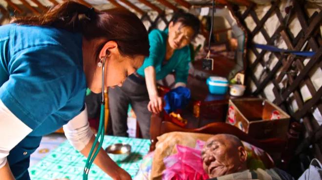 Female health care worker with stethoscope caring for an elderly patient at his home in Ulaanbaatar