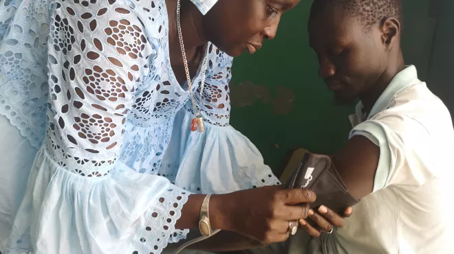 Female community health worker measuring blood pressure of a boy in Dakar