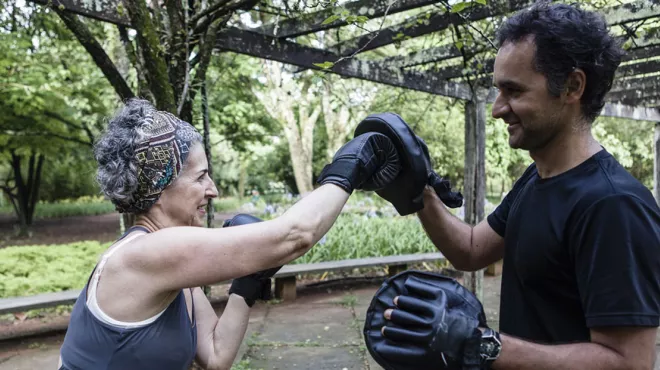 Woman with trainer, practicing boxing outside in front of trees