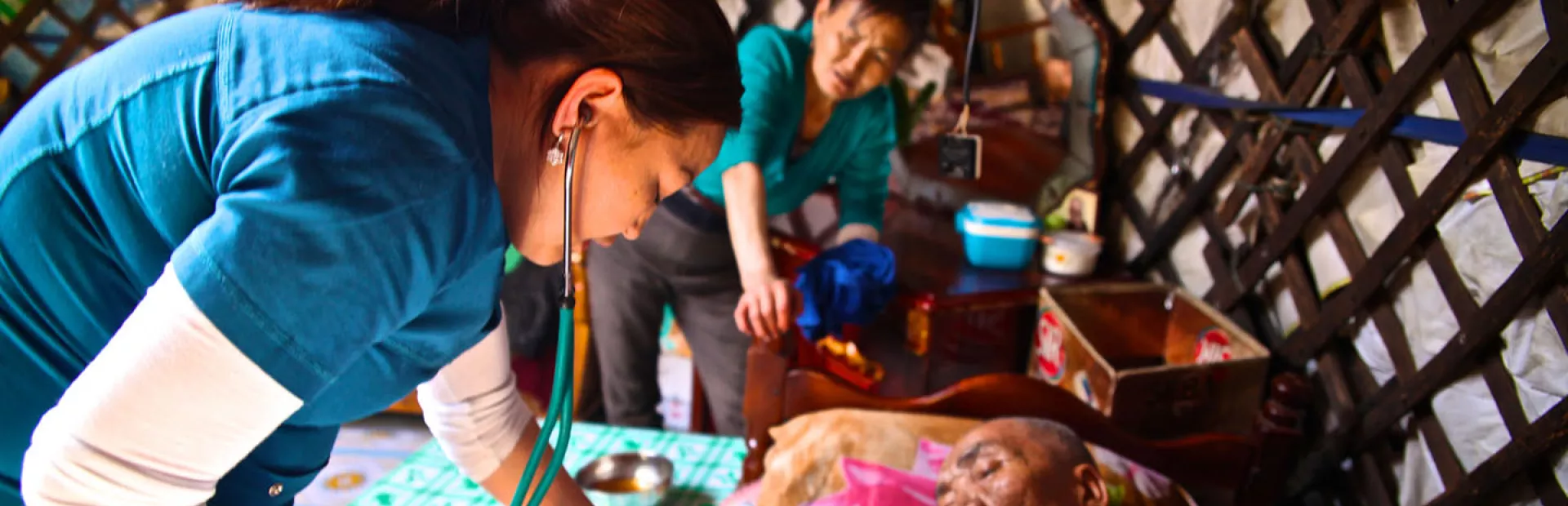Female health care worker with stethoscope caring for an elderly patient at his home in Ulaanbaatar